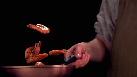 SUPER-SLOW-MOTION-Professional-female-cook-prepares-shrimps.-Throwing-and-flipping-scampi-on-pan.-Cooking-seafood,-healthy-vegetarian-food-on-a-dark-background.-Shot-with-high-speed-camera,-420-FPS